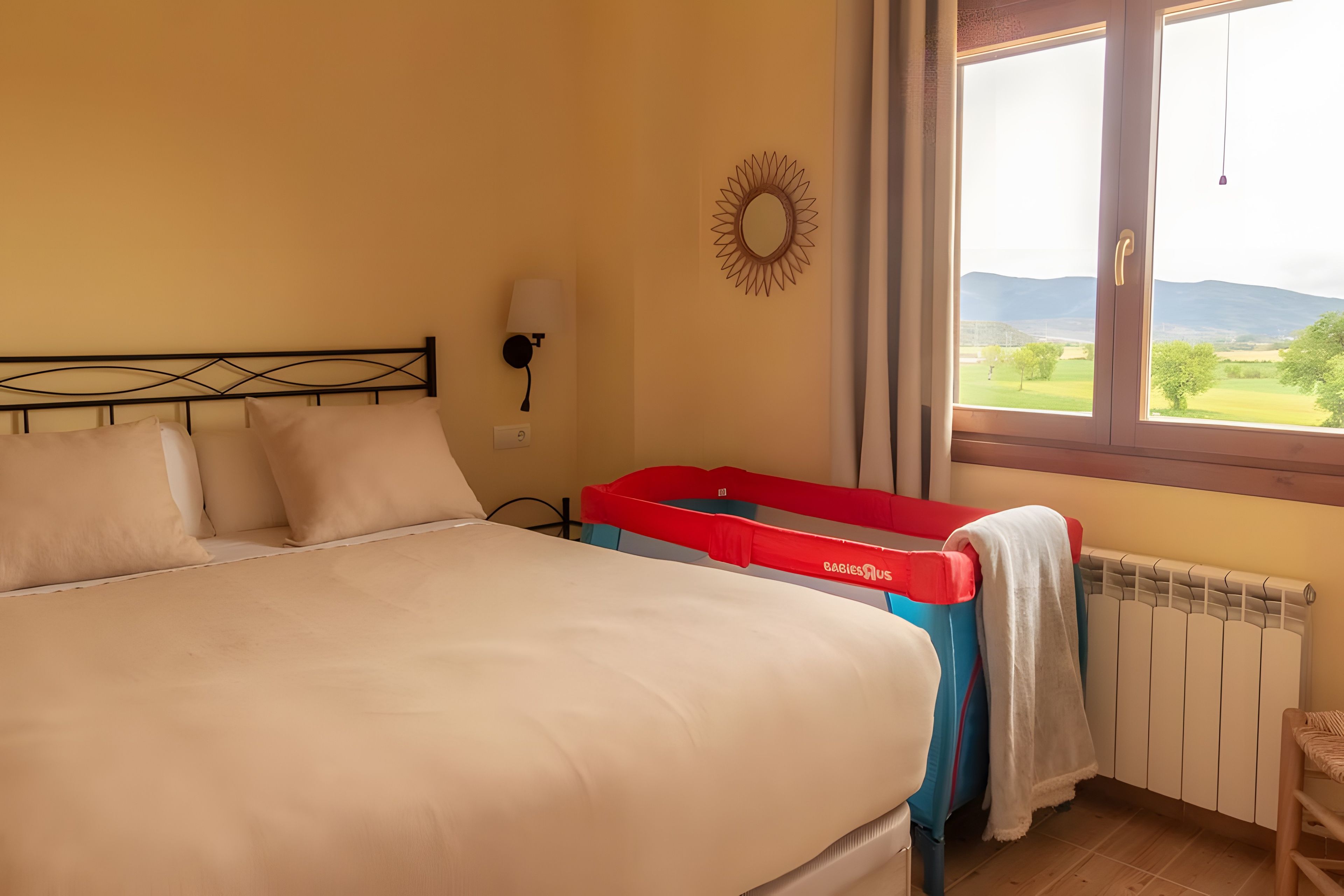 Un dormitorio con cama, ventana con vistas al campo y lámpara de pared.