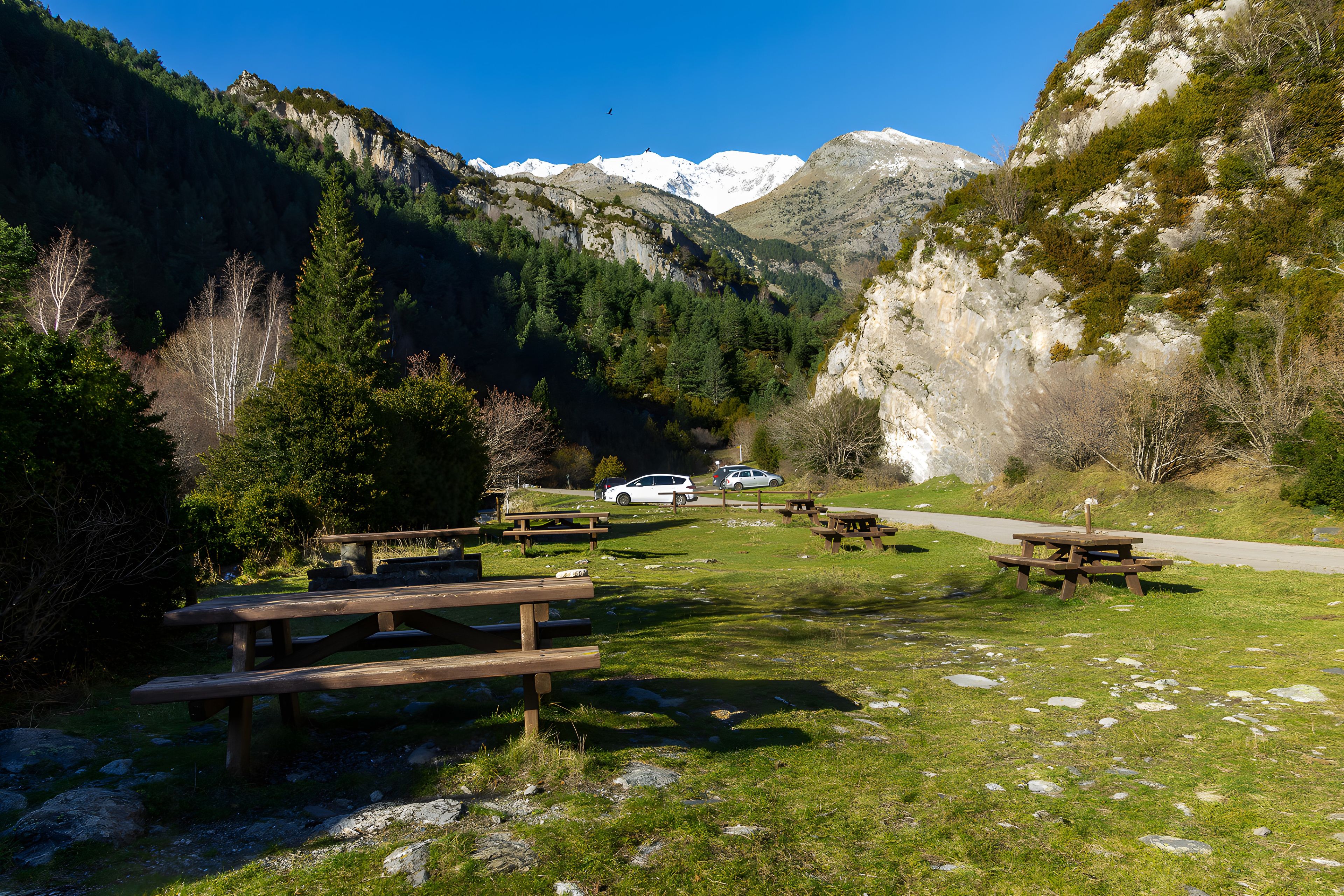 Paisaje montañoso con mesas de picnic y una carretera con coches estacionados.