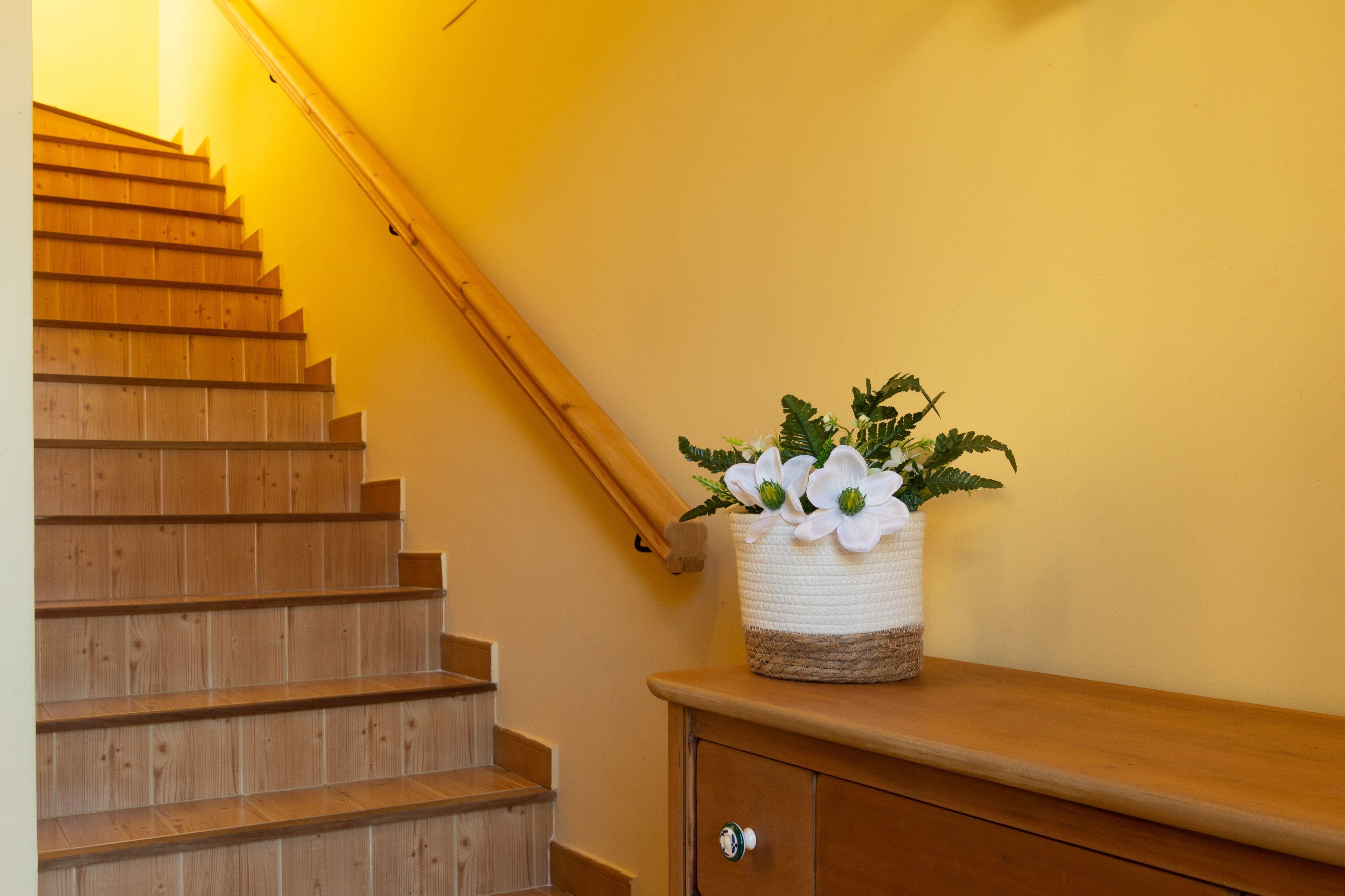 A wooden staircase with a basket of white flowers on a wooden bench.