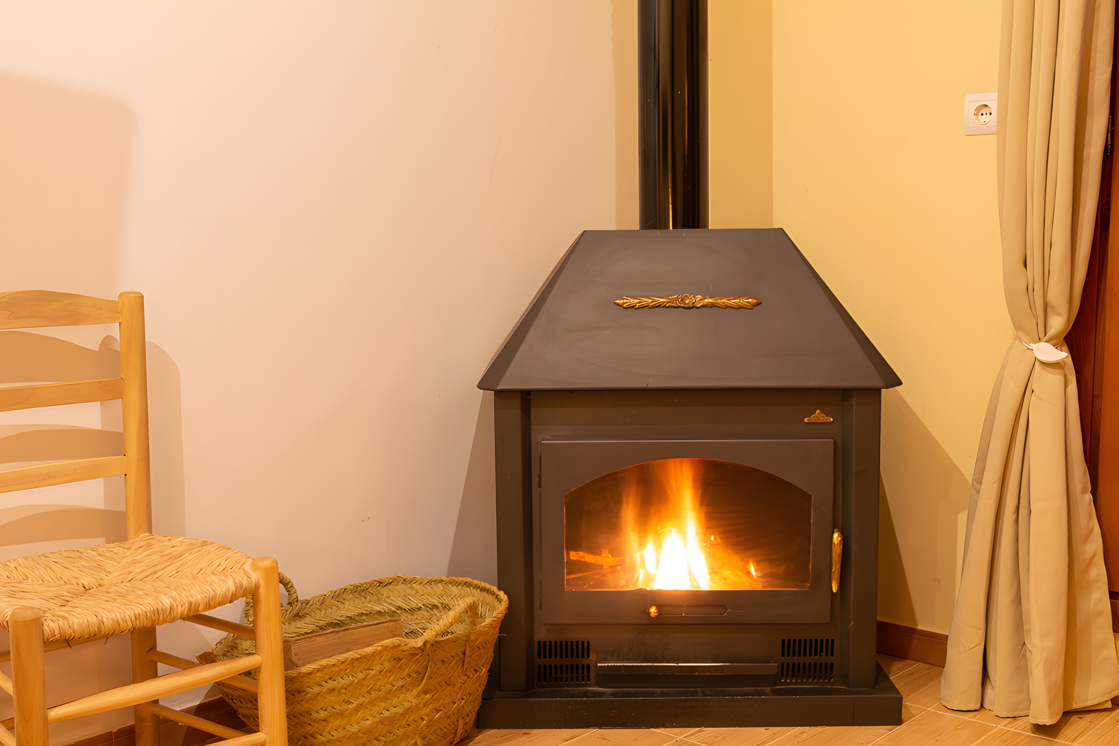 Una habitación con una estufa de leña, una silla de madera y una cesta tejida.