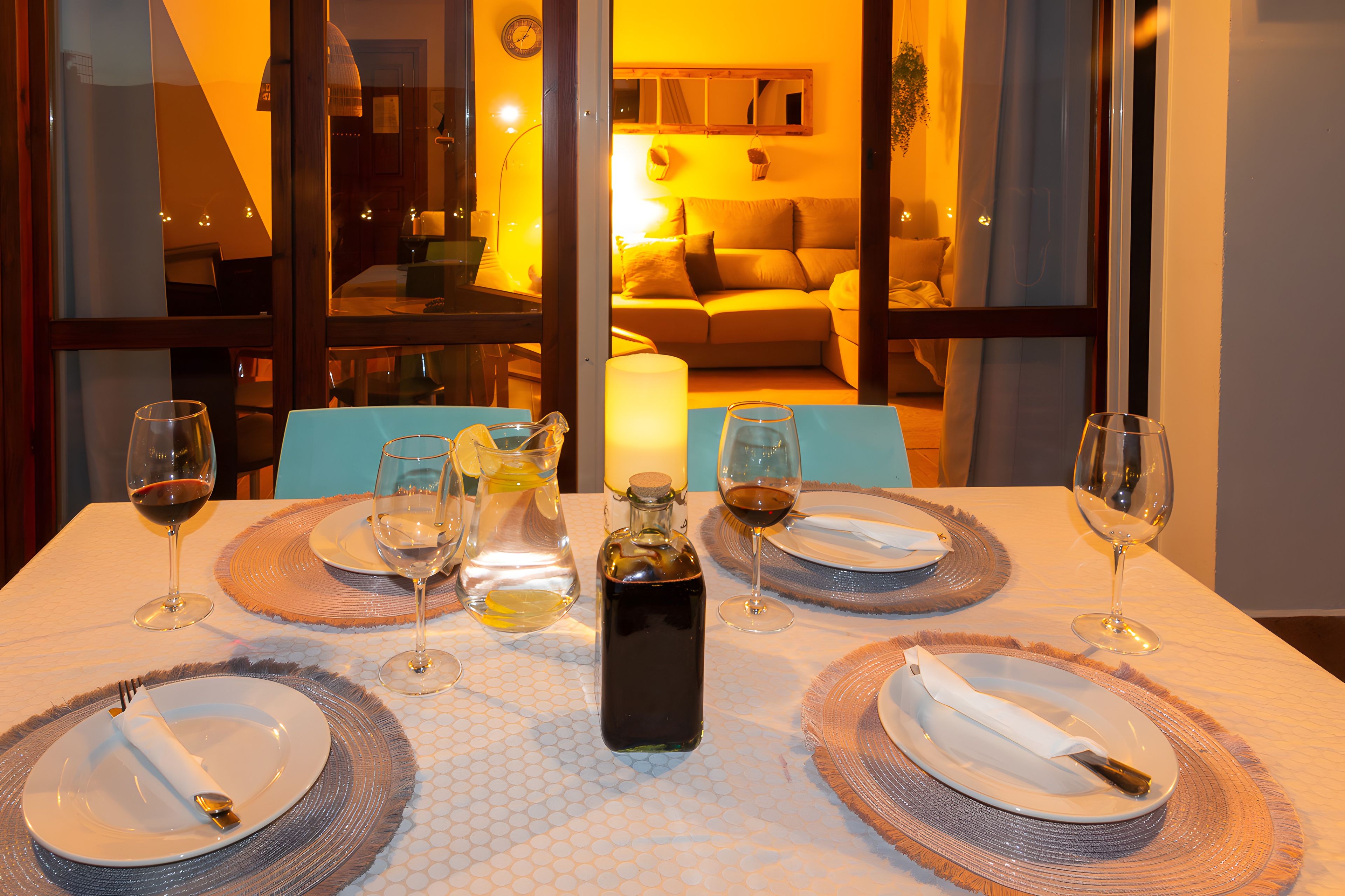 Una mesa de comedor lista para cuatro, con copas de vino, platos y una botella.