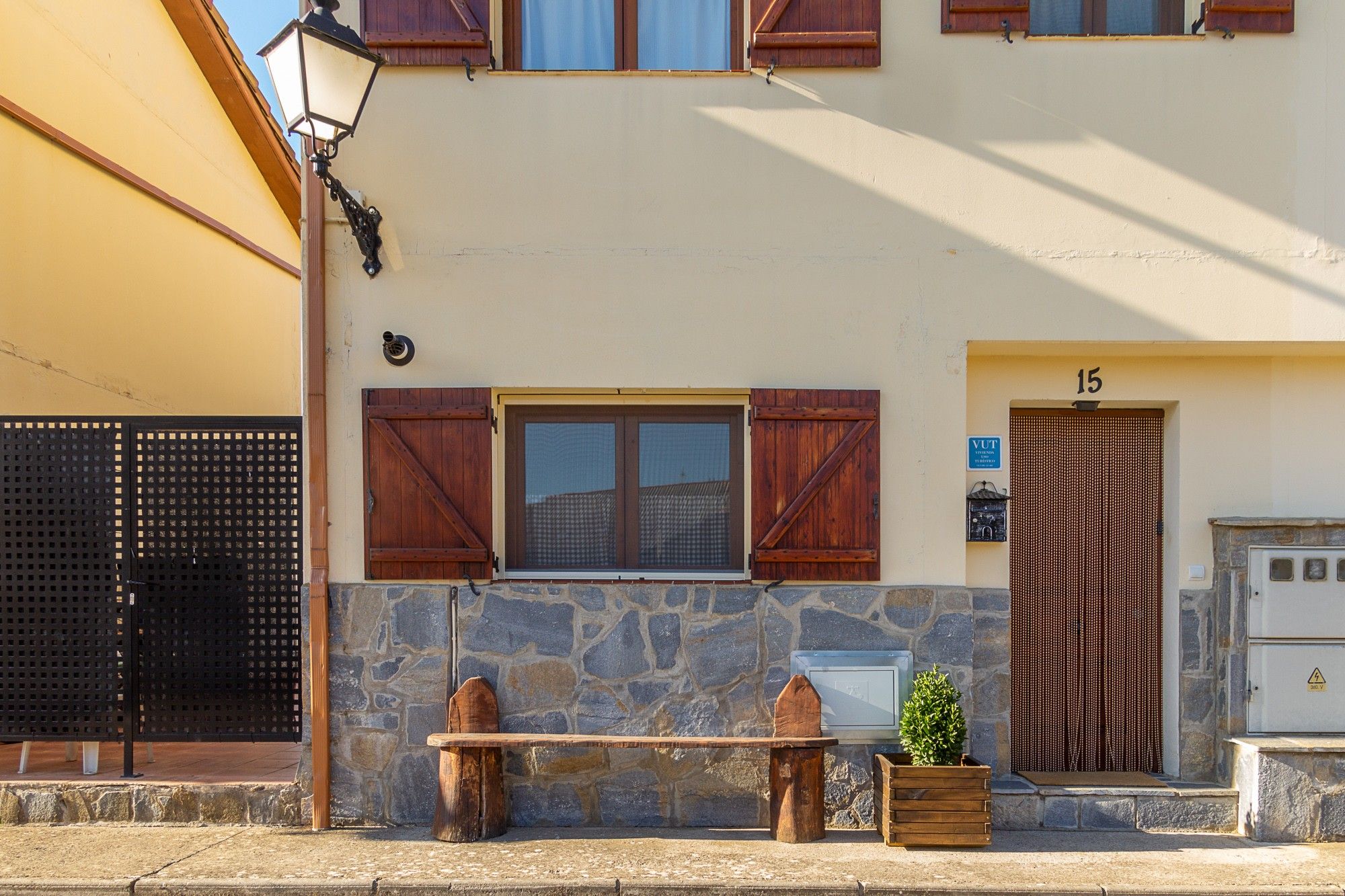 Un edificio con fachada de piedra, contraventanas de madera y un pequeño banco afuera.