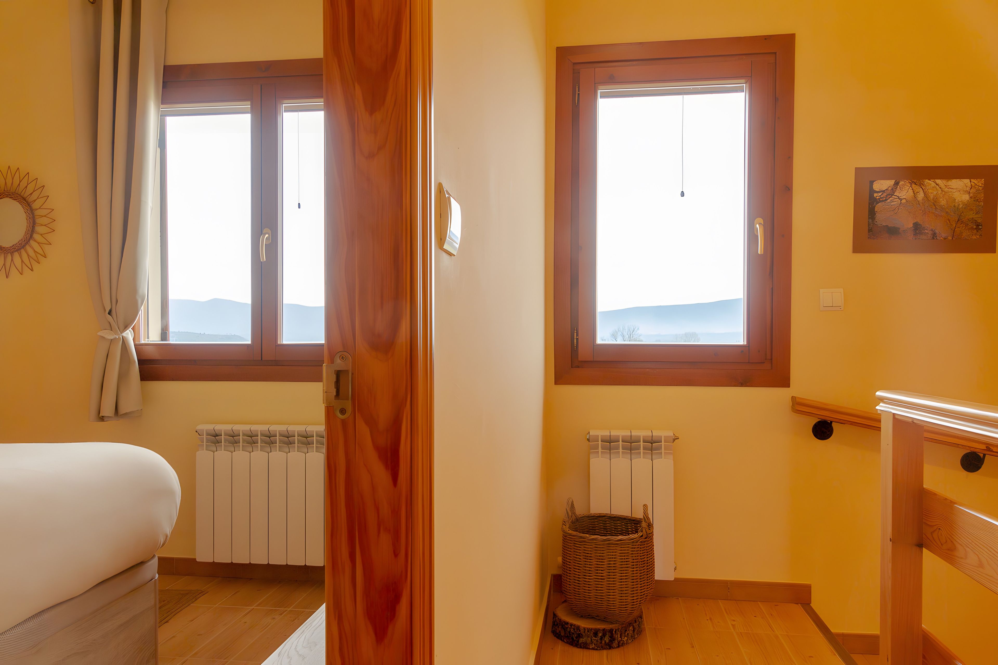 Un dormitorio con una cama, dos ventanas, un radiador y un cuadro colgado en la pared.