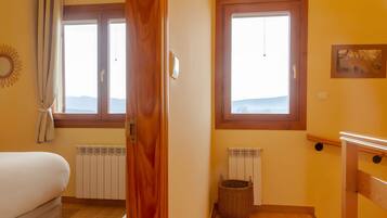 Un dormitorio con una cama, dos ventanas, un radiador y un cuadro colgado en la pared.
