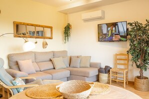 A living room with a sofa, chairs, a television, a plant, and a wall-mounted air conditioner.