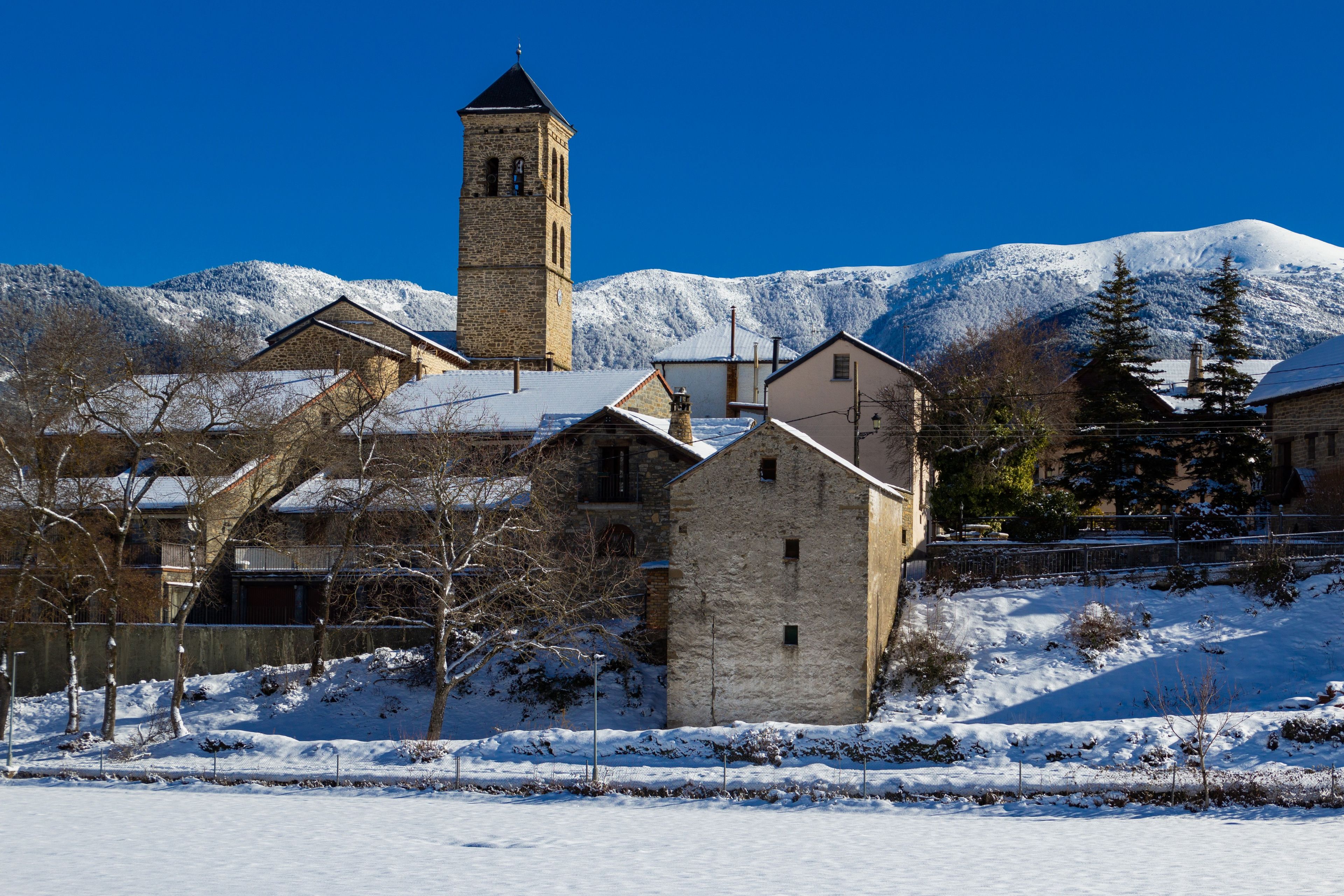 A snow-covered village with traditional stone buildings and a prominent church tower.