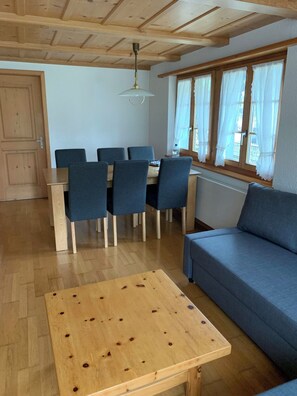 A living room with a wooden ceiling, a dining table with chairs, a sofa, and a window with curtains. - Alpenglühn Appartement/Fewo, Bad, WC, 3 Schlafräume by Interhome (Adelboden)
