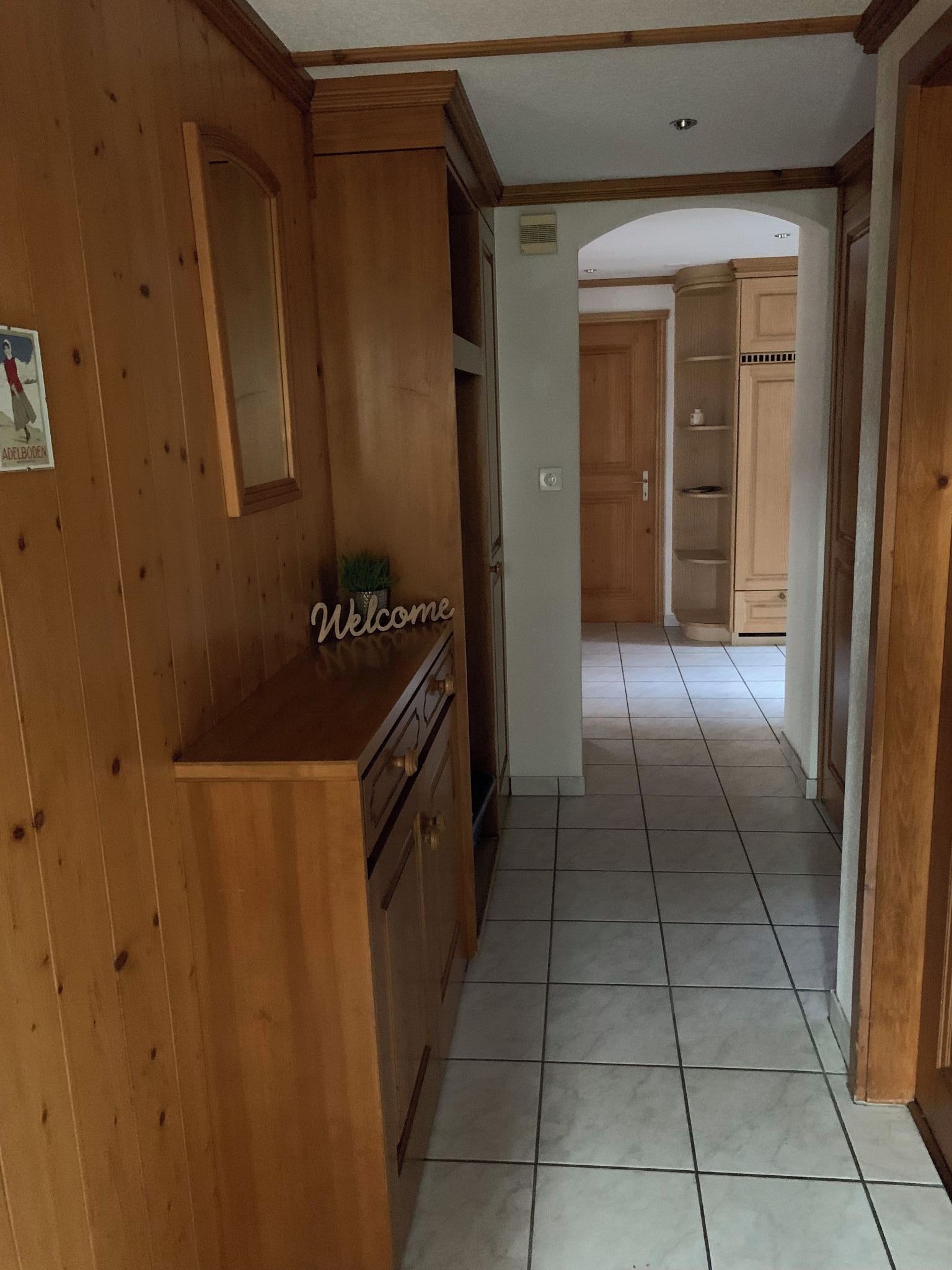 A wooden interior hallway with a welcome sign, a potted plant, and a tiled floor.