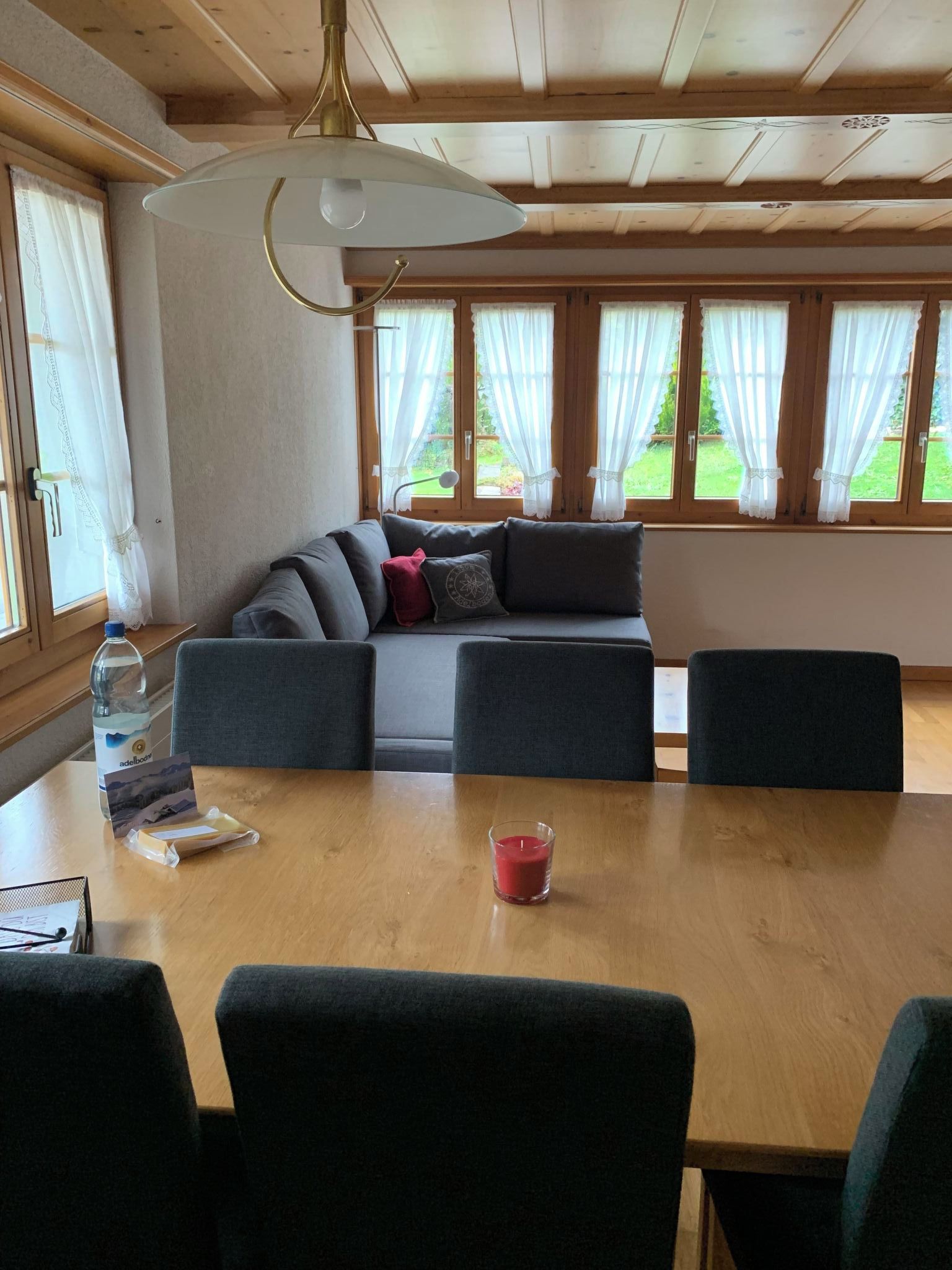Une pièce avec un plafond en bois, un canapé avec des coussins, une table avec des chaises et des fenêtres avec des rideaux.