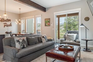 A modern living room with a grey sofa, a leather ottoman, and a dining area with a table and chairs. - Luxury Grand Park Retreat with Private Hot Tub (Fraser)