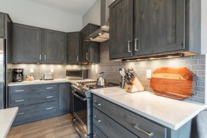 Una cocina moderna con armarios oscuros, una estufa de acero inoxidable, un microondas y una tabla de cortar de madera.