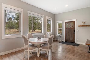 A dining area with a round table and four chairs, large windows, a wooden floor, and a door with a bull head decoration. - Luxury Grand Park Retreat with Private Hot Tub (Fraser)