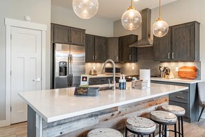 A modern kitchen with a large island, stainless steel appliances, and a brick backsplash. - Luxury Grand Park Retreat with Private Hot Tub (Fraser)