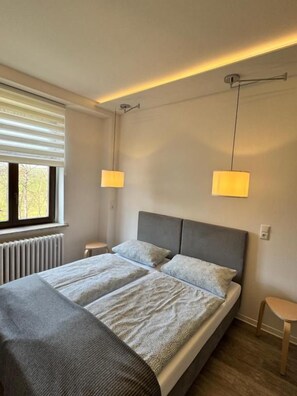 A modern bedroom with a large bed, bedside tables, and a window with blinds. - Landgasthof & Pension Waldeck (Treuen)