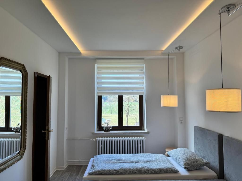 A bedroom with a bed, a window with blinds, a radiator, and a hanging lamp.