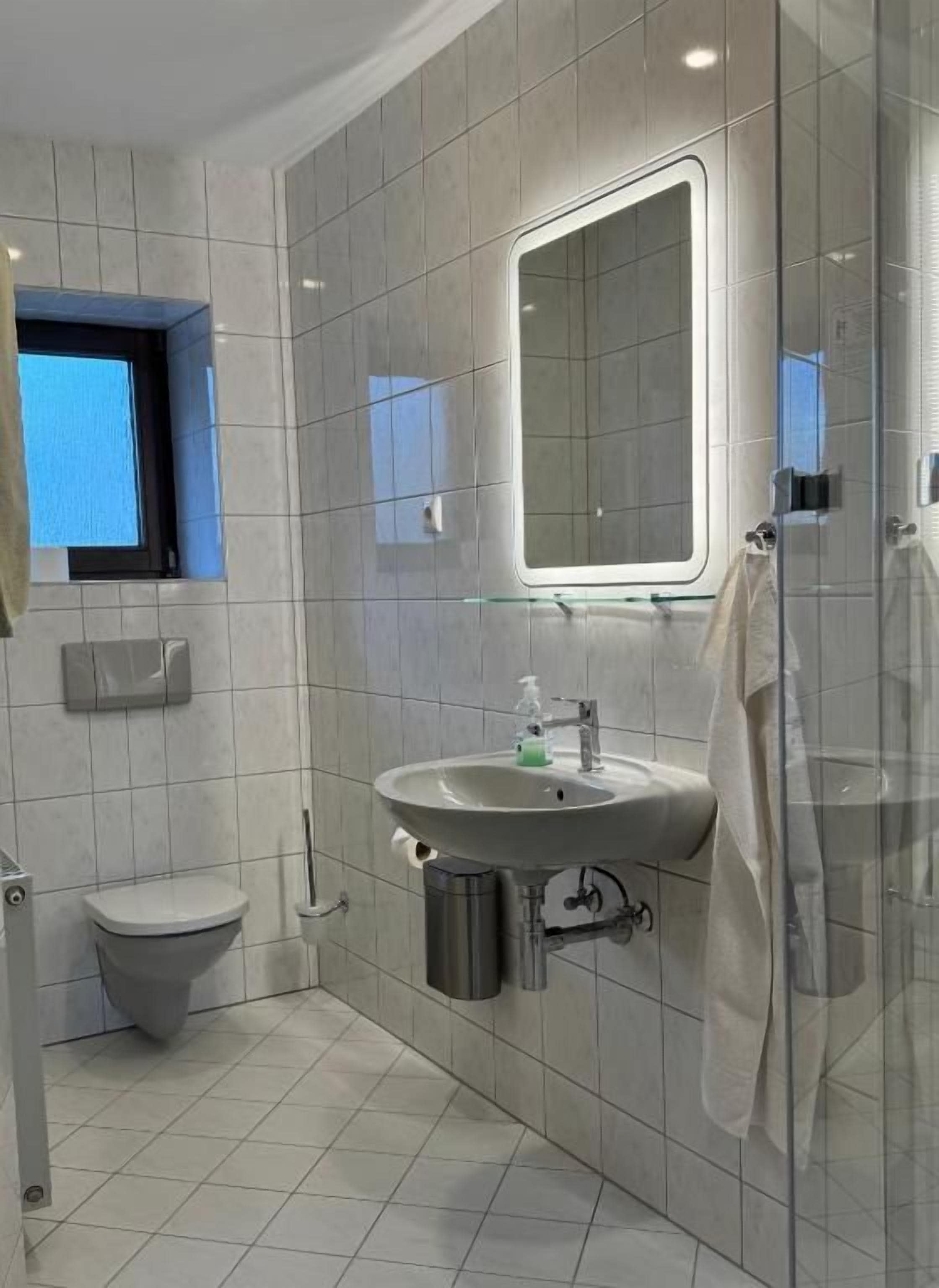Un baño con lavamanos, espejo, inodoro y ventana.