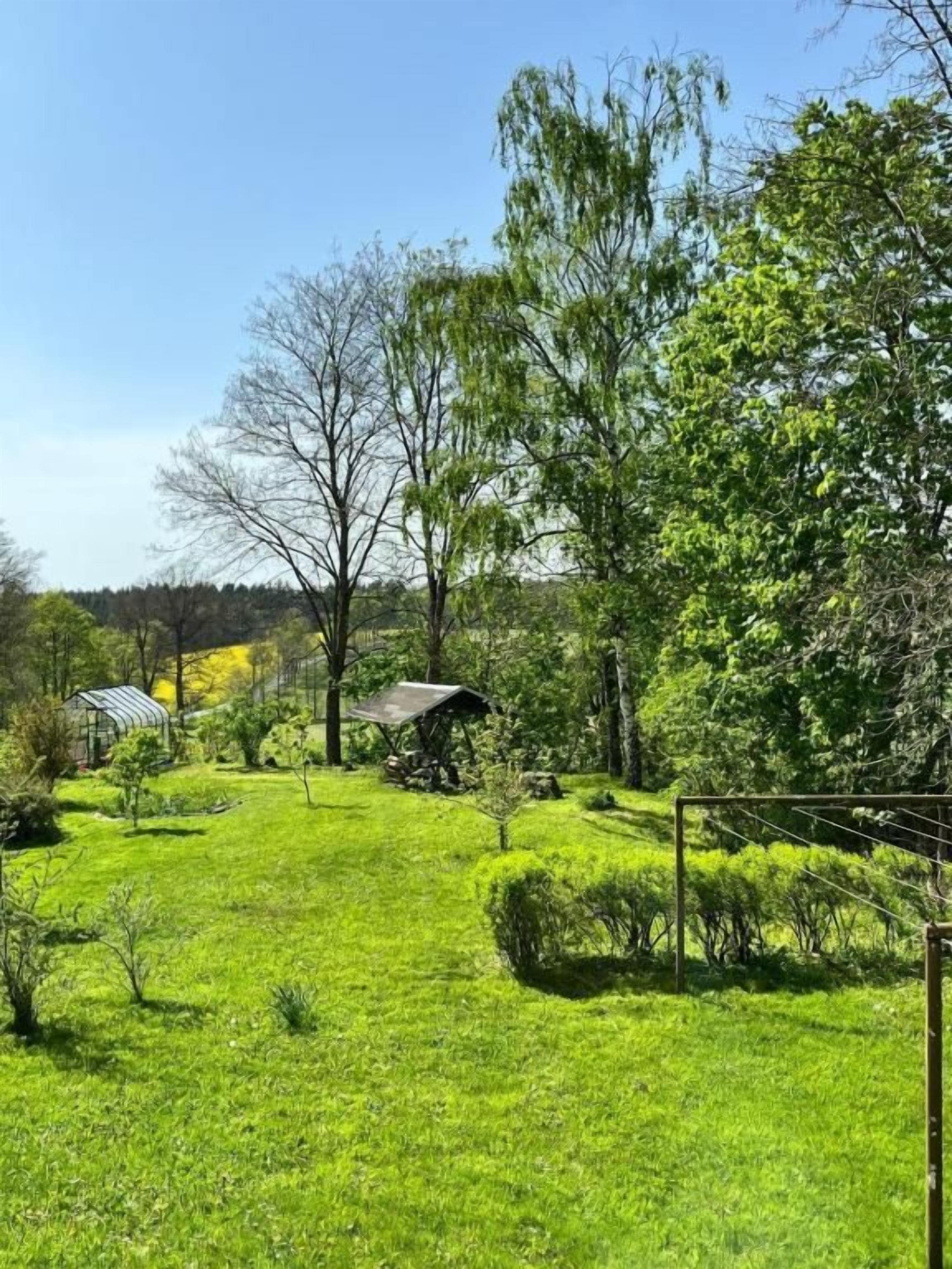 Ein üppiger, grüner Garten mit verschiedenen Bäumen und Sträuchern, einer kleinen Struktur und einem eingezäunten Bereich.