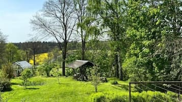 Ein üppiger, grüner Garten mit verschiedenen Bäumen und Sträuchern, einer kleinen Struktur und einem eingezäunten Bereich.