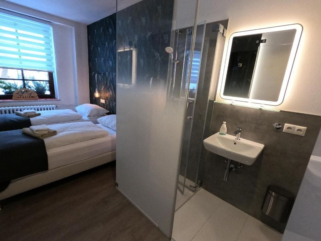 Ein modernes Schlafzimmer mit Bett, Nachttisch, Fenster mit Jalousien und einer Duschkabine mit Glastür.
