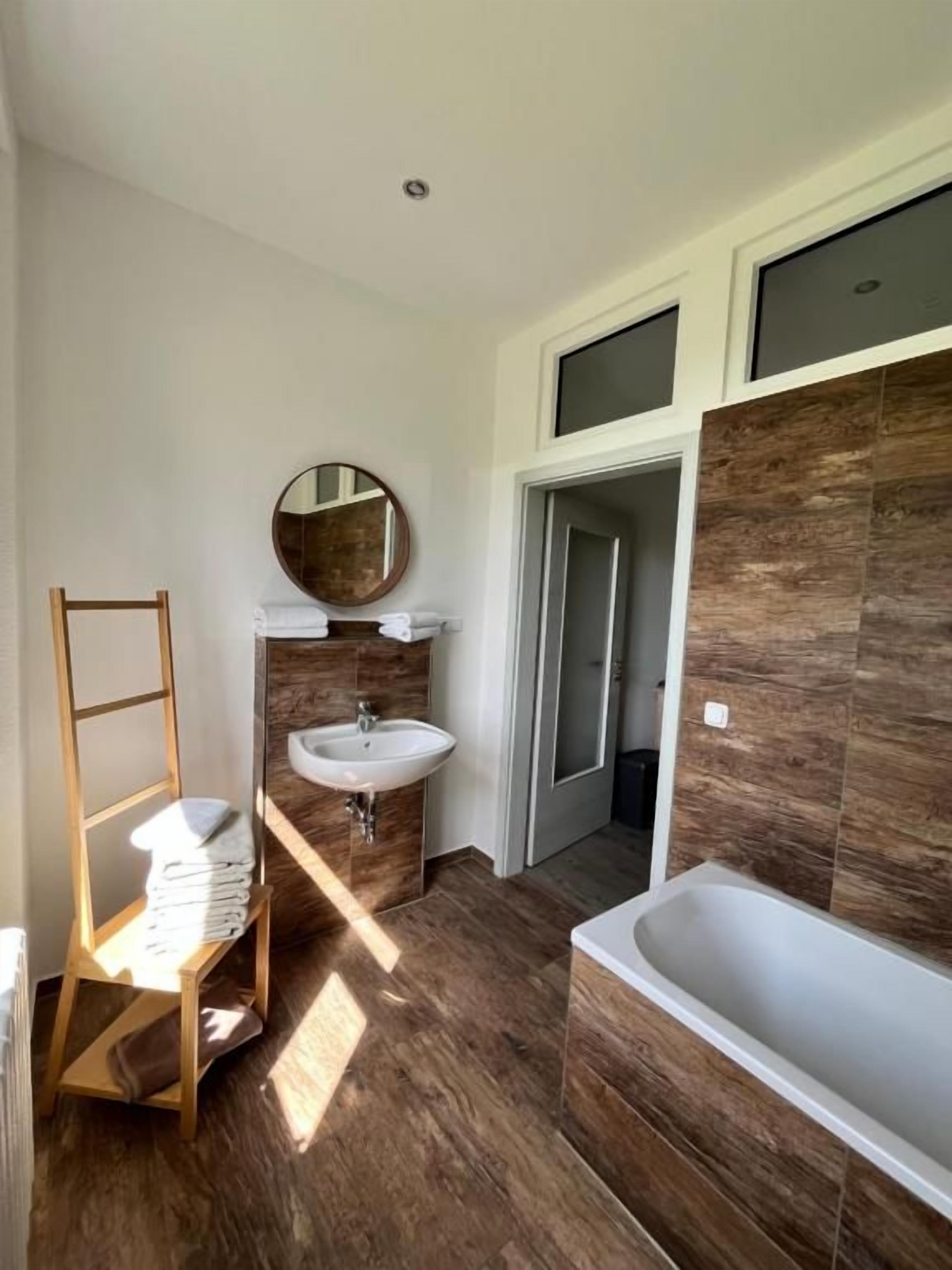 Ein Badezimmer mit Holzboden, Waschbecken, Spiegel und Badewanne.