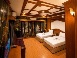 Quarto de hotel com teto de madeira, duas camas com roupa de cama branca, um sofá de couro, uma TV e uma janela com cortinas.
