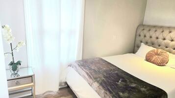 A neatly made bed with a tufted headboard, a bedside table with a drawer, and a potted orchid.
