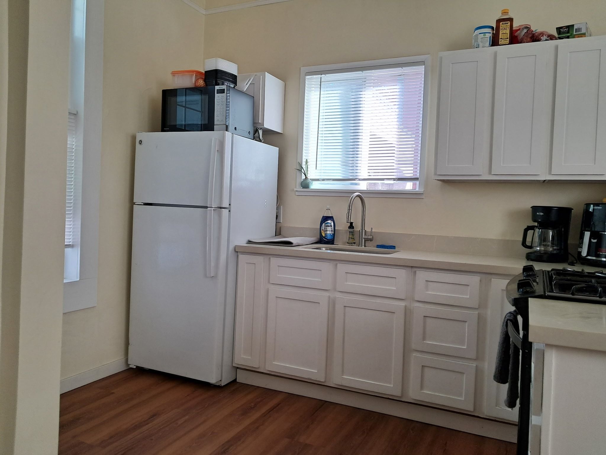 A compact kitchen with white cabinets, a refrigerator, a sink, and a window with blinds.