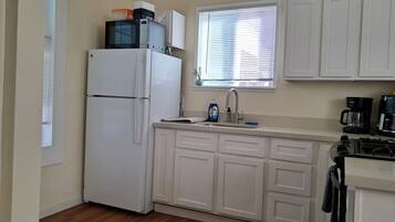 A compact kitchen with white cabinets, a refrigerator, a sink, and a window with blinds.