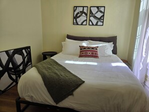 A bed with white bedding, a green throw blanket, and a decorative pillow. There are two wall-mounted artworks above the bed. - Sunny Two Bedroom in Uptown  (Oakland)