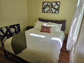 A bed with white bedding, a brown headboard, and a patterned pillow. There are two framed artworks on the wall above the bed. - Sunny Two Bedroom in Uptown  (Oakland)
