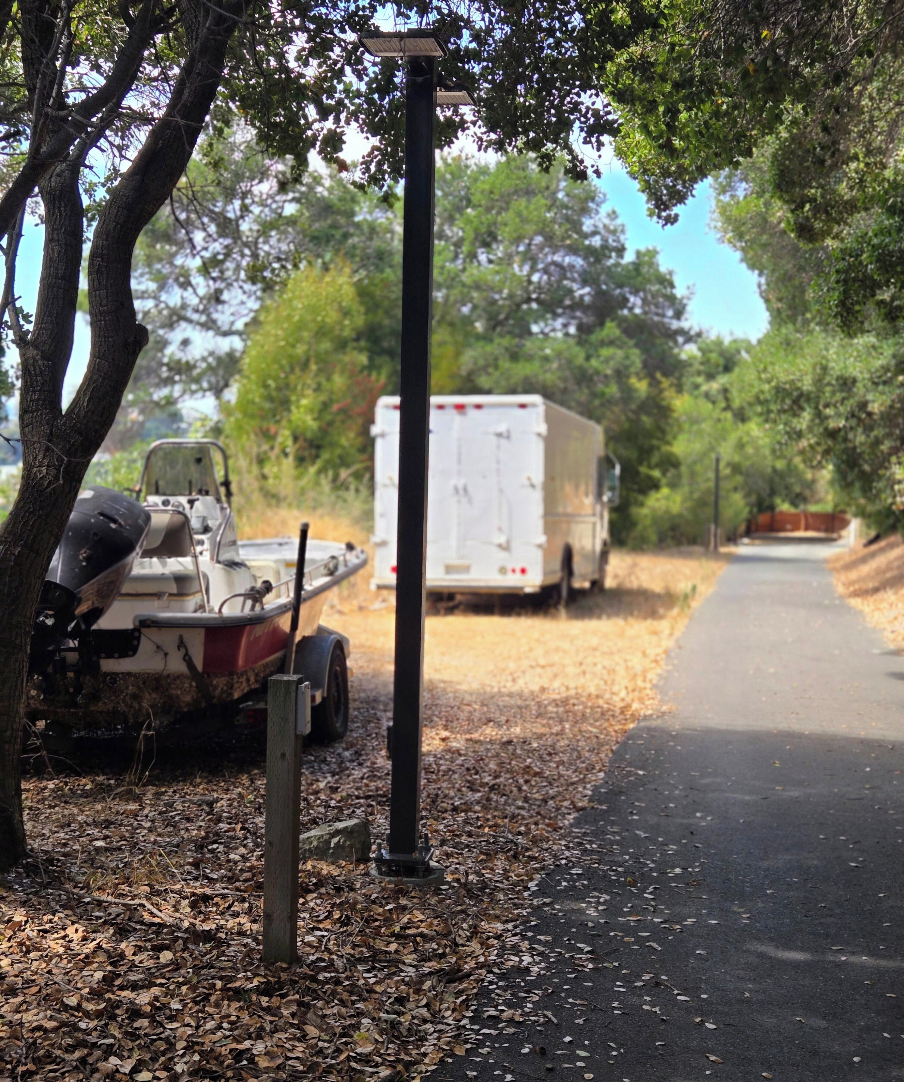 A paved road with a boat and a trailer on the left and a white truck on the right.