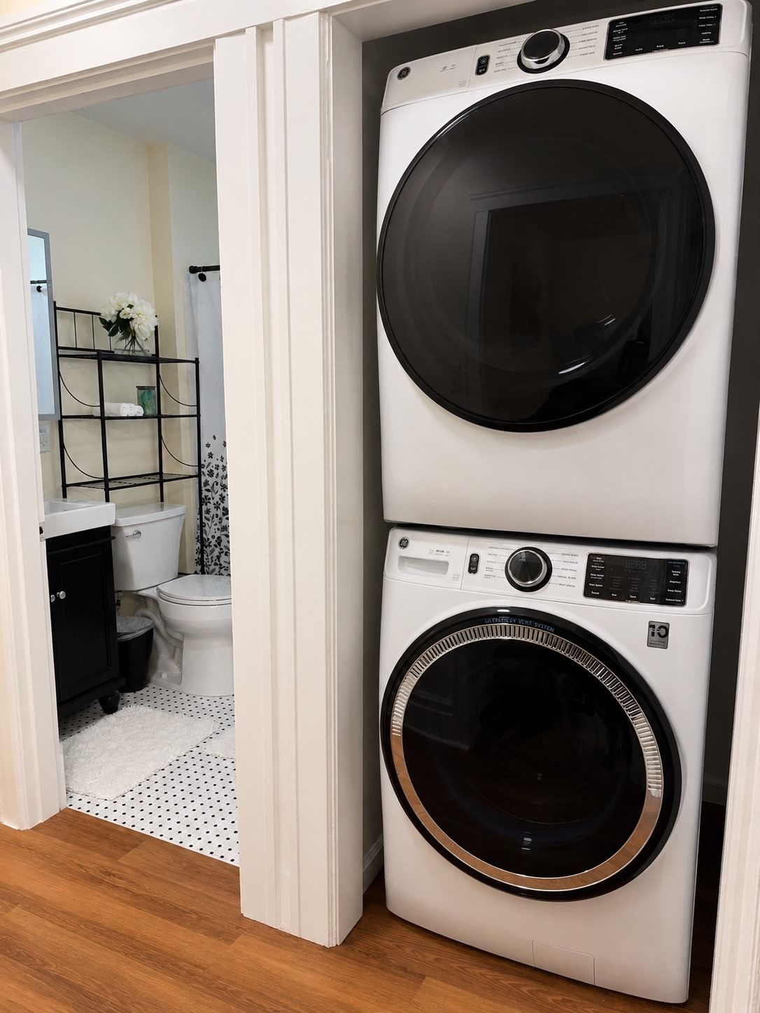 A compact laundry room with a stacked washer and dryer, a white toilet, and a small shelf with a vase.