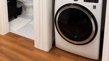 A compact laundry room with a stacked washer and dryer, a white toilet, and a small shelf with a vase.