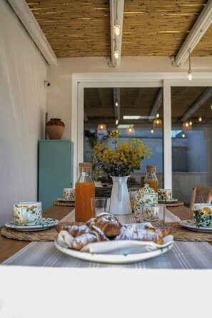 Ein Essbereich im Freien mit einem Tisch, gedeckt für ein Frühstück, darunter Gebäck, eine Karaffe Orangensaft und eine Vase mit Blumen.