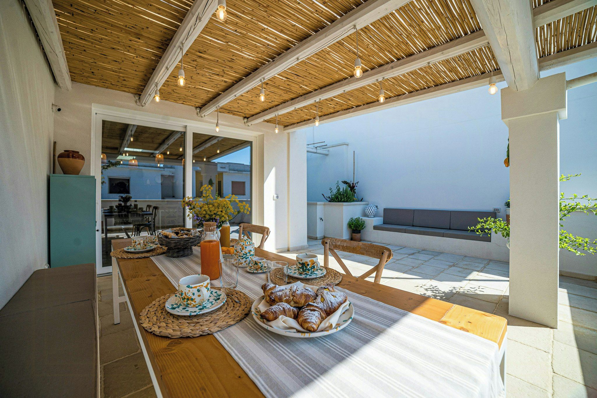 Un espace de restauration en plein air avec une table dressée pour le petit-déjeuner, comprenant des viennoiseries et une bougie.