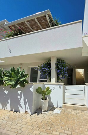 Ein modernes, zweistöckiges Haus mit weißer Fassade, einer überdachten Terrasse und Topfpflanzen.