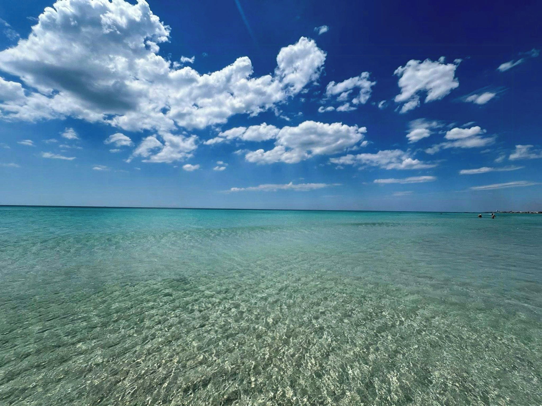 A clear blue sky with scattered clouds over a calm sea.