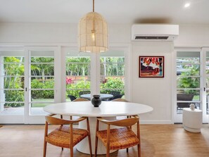 A round dining table with four chairs, a hanging light fixture, and a view of a lush garden through large glass doors. - Lanikai Monthly Home, Private Guest Suite, 2 Parking, and Walk to Beach (Kailua)