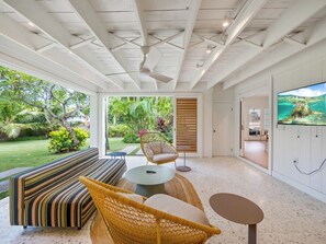 A spacious room with a large window, a ceiling fan, a sofa, a chair, a small round table, and a television. - Lanikai Monthly Home, Private Guest Suite, 2 Parking, and Walk to Beach (Kailua)
