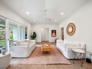 A spacious living room with white sofas, a central coffee table, and a large window providing a view of the outdoors. - Lanikai Monthly Home, Private Guest Suite, 2 Parking, and Walk to Beach (Kailua)