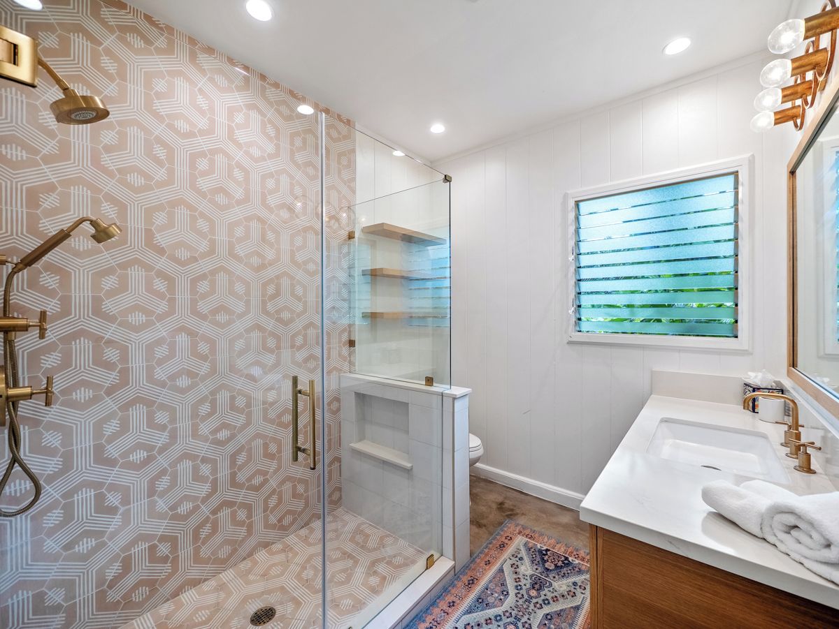 Casa de banho com cabine de chuveiro em vidro, lavatório branco e janela com persianas.
