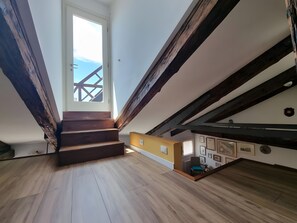 Eine Treppe führt zu einer Schlafgalerie mit Holzbalken und Blick zum Himmel.