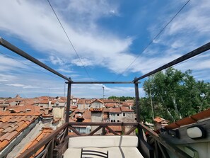 Ein Balkon mit Blick auf Gebäude mit Terrakotta-Dächern und einem wolkenlosen Himmel.