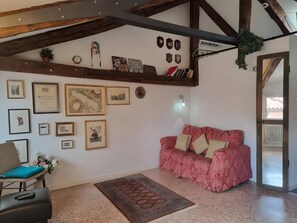 Ein Zimmer mit einem roten, gemusterten Sofa, einer Holzbalkendecke und verschiedenen gerahmten Bildern an den Wänden.