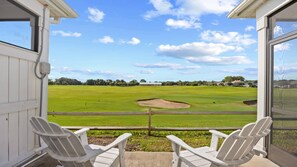Blick von einer Veranda mit zwei Adirondack-Stühlen auf einen Golfplatz.