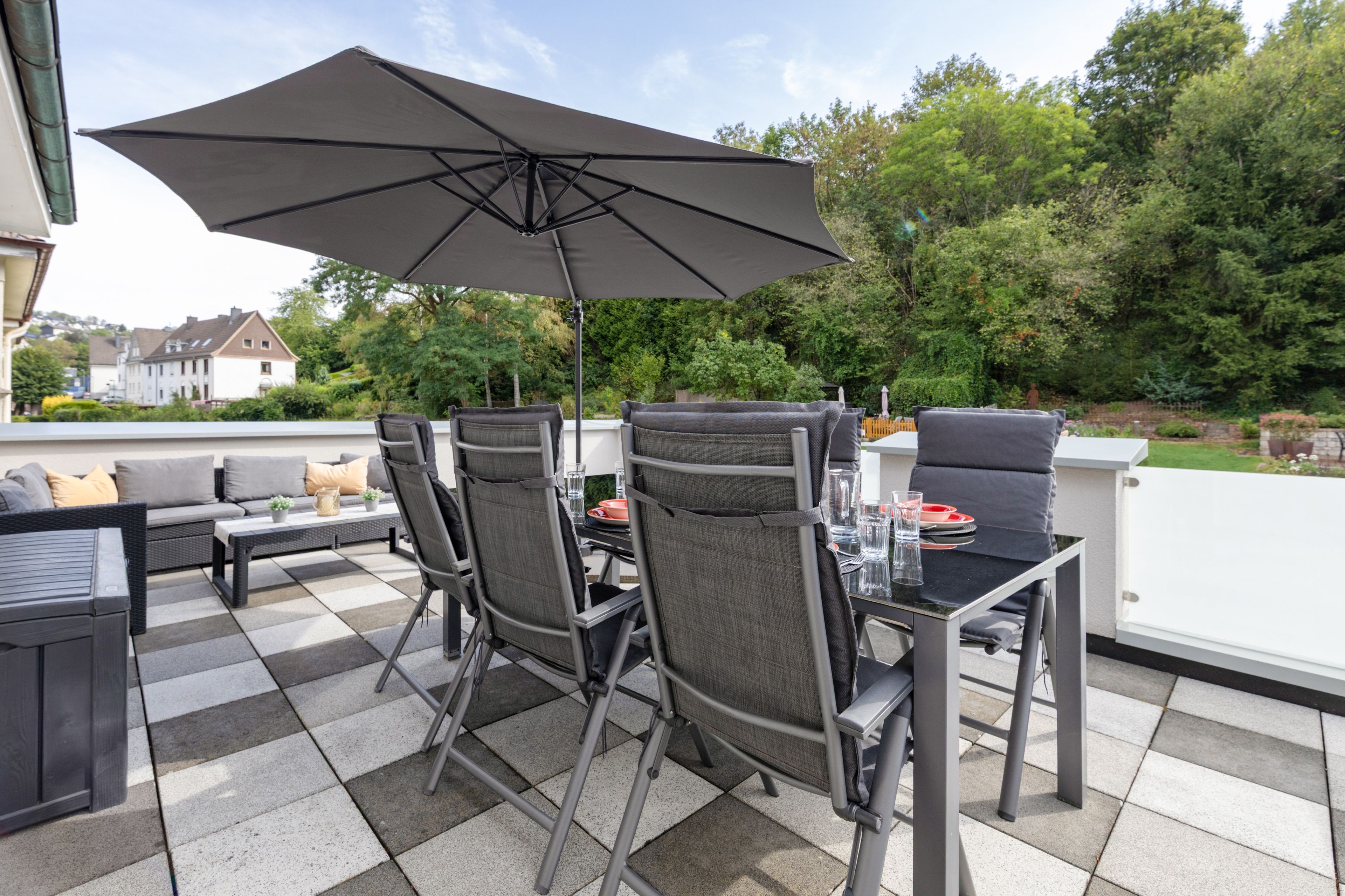 En udendørs patio med et spisebord, omgivet af stole og en parasol.