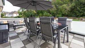 En udendørs patio med et spisebord, omgivet af stole og en parasol.