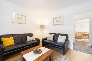 A modern living room with two black leather sofas, a wooden coffee table, and a floor lamp. There are framed pictures on the walls and a clock on the door. - Apartment “Welcome” with Private Rooftop Terrace (Olpe)