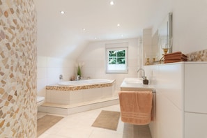 Un baño moderno con una bañera independiente, un tocador con espejo y un ventanal que proporciona luz natural.
