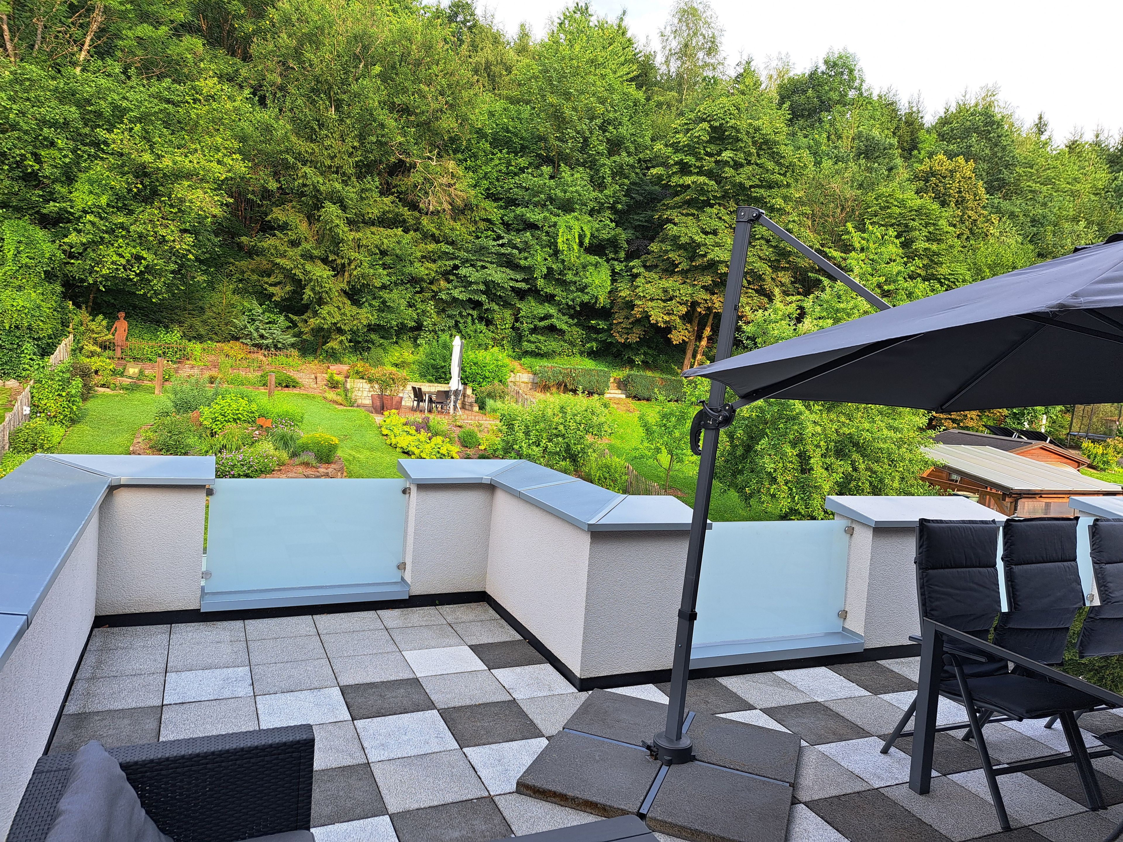 Una terraza en la azotea con piso a cuadros, mobiliario exterior y vistas a un jardín exuberante.